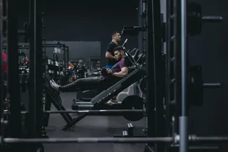 Homme assis sur une machine de leg extension, galet posé au bas du tibia, en salle de sport